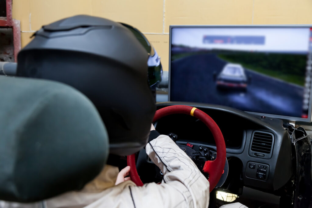A professional racer in a black helmet and a white homologated suit sits in the sports seat of a car for drifting and racing during a race and training on a simulator.